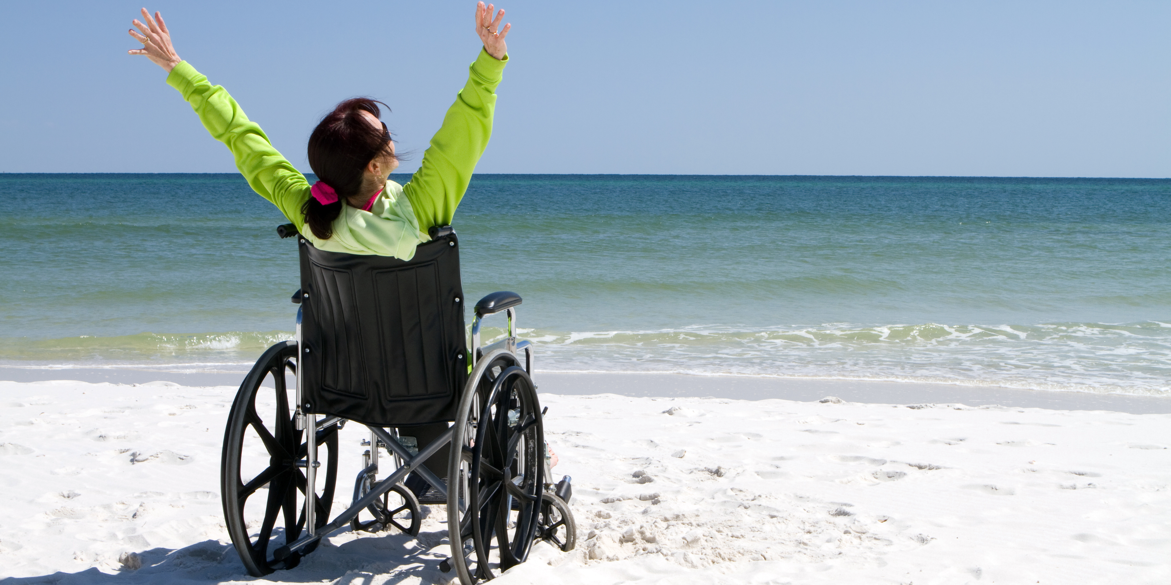 Person in wheelchair sitting on the beach and raising arms happily.